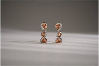 Two-tone hoop earrings with an infinity twist design, featuring pavé-set lab-grown diamonds, resting on a white surface.