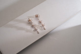 Two-tone dangle earrings with a cascading flower design set with lab-grown diamonds, lying on a white curved surface with shadows.