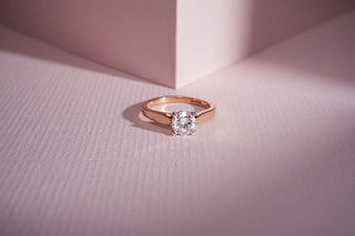 rose gold lab-grown diamond engagement ring placed on a light pink surface with a light pink sheet in the background