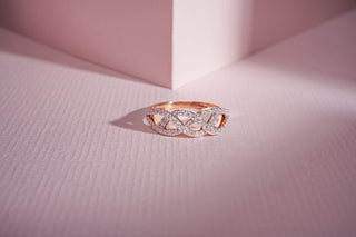 A rose gold lab-grown diamond ring with an twist design and pavé-set stones rests on a light pink textured background.