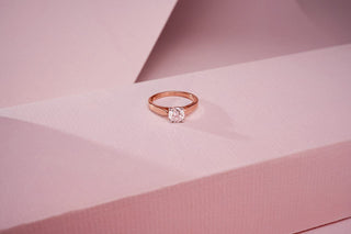 rose gold lab-grown diamond engagement ring placed on a light pink surface with a light pink background