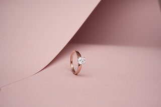 lab-grown diamond ring with a rose gold band placed beside a light pink sheet with a light pink background