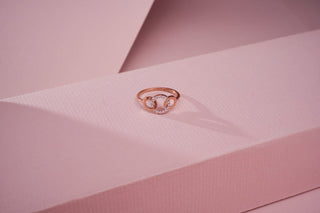 lab-grown diamond ring with a rose gold band placed on a light pink cardboard with a light pink background 