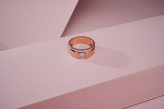rose gold lab-grown diamond engagement ring placed on a light pink surface with a light pink sheet in the background