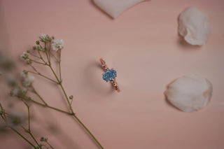 blue coloured lab-grown diamond engagement ring with a rose gold band placed amidst flower petals with a light pink background