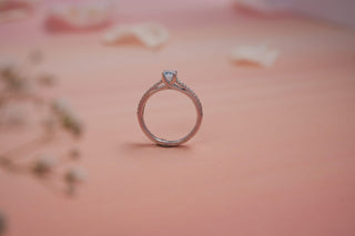 blue coloured lab-grown diamond engagement ring with a white gold band placed amidst flower petals with a light pink background