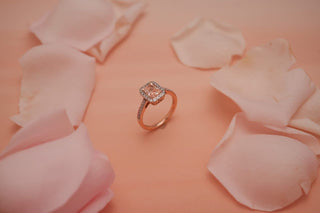 pink coloured lab grown diamond with a rose gold band placed amidst light pink petals with a light pink background
