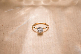 Yellow gold solitaire lab grown diamond ring on a beige surface