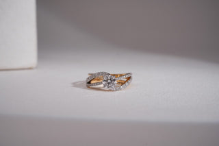 A two-tone crossover ring with a round central lab-grown diamond and pavé bands rests on a clean white surface