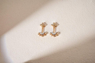 A pair of gold ear jackets with floral and crescent designs, set with lab-grown diamonds, rests on a white surface.