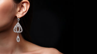 Close-up of a woman wearing an intricate, teardrop-shaped lab-grown diamond earring by Réia Diamonds, set against a black background.