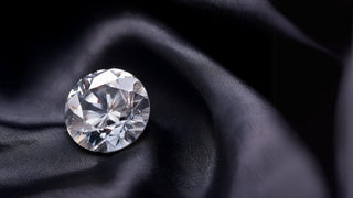 A close-up of a brilliant round-cut lab-grown diamond from Réia Diamonds, resting on a luxurious black silk fabric.