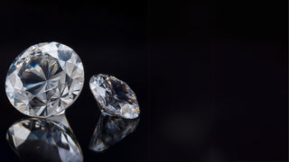 Two brilliant, round-cut loose lab-grown diamonds from Réia Diamonds, shown with their reflections on a dark, polished surface