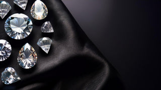Various cuts of loose lab-grown diamonds from Réia Diamonds sparkle on a luxurious black satin fabric.