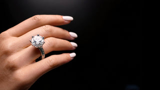 Close-up of a hand wearing a diamond ring from Réia Diamonds, featuring a large central diamond and a sleek band.