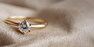 A Réia yellow gold solitaire ring with a six-prong setting and a round lab-grown diamond, resting on beige fabric.