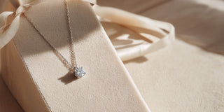 A timeless Réia white gold solitaire necklace, centered with a brilliant round lab-grown diamond, presented on a beige  display.