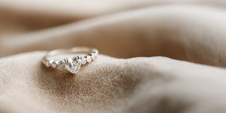 A Réia white gold ring featuring a heart-shaped lab-grown diamond center stone flanked by round lab-grown diamonds, resting on beige fabric.