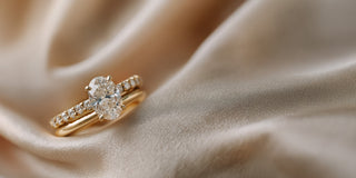 A Réia yellow gold engagement set with an oval lab-grown diamond and a matching lab-grown diamond eternity band, resting on draped satin fabric.