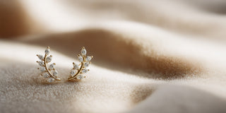 Yellow gold lab-grown diamond earrings, shaped like curved branches with marquise stones, rest on soft, folded beige fabric.