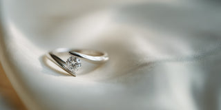 A Réia white gold solitaire ring with a round lab-grown diamond in a tension setting, resting on draped pale neutral satin fabric.