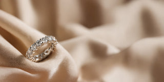 A Réia white gold eternity band ring set with round lab-grown diamonds, resting on beige fabric.