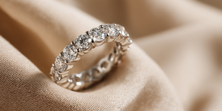 Reia white gold eternity band featuring large, round lab-grown diamonds in a prong setting, resting on a beige fabric.