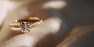A Réia yellow gold engagement ring with a round lab-grown diamond on a pavé diamond band, resting on beige fabric.