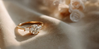 A Réia yellow gold three-stone ring with lab-grown diamonds, resting on beige fabric with blurred flowers.