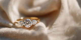 A Réia yellow gold three-stone ring, featuring a round center lab-grown diamond flanked by two pear-shaped lab-grown diamonds, resting on soft fabric.