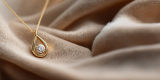 Réia yellow gold teardrop pendant necklace with a floating lab-grown diamond, displayed on champagne fabric.
