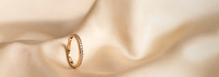 A Réia yellow gold eternity band ring set with channel-set lab-grown diamonds, resting on beige fabric.