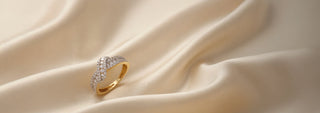 A Réia rose gold ring with a cluster of round lab-grown diamonds, resting on beige sand and fabric.
