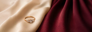A Réia yellow gold three-stone ring with a central Emerald-cut lab-grown diamond and two round lab-grown diamond side stones, resting on beige fabric with dried flowers.