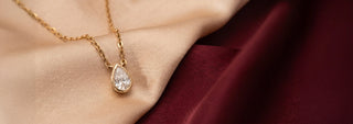 A yellow gold lab-grown diamond ring features an emerald cut stone flanked by marquise accents, on beige silk near dry flowers.