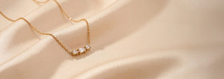 Top view of a lab-grown diamond bar necklace in 14 KT yellow gold, featuring an emerald-cut centre diamond flanked by two bezel-set radiant-cut diamonds on a delicate chain.