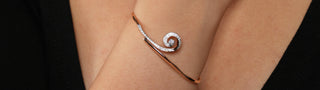 A thin rose gold cuff bracelet with a lab-grown diamond spiral design on an arm.