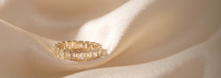 A Réia white gold eternity band ring set with round lab-grown diamonds, resting on beige fabric.