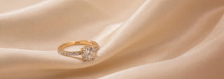 Réia yellow gold solitaire ring with a pavé lab-grown diamond band, resting on beige fabric.