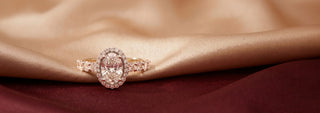 A Réia yellow gold ring with a round lab-grown diamond center stone and a diamond halo, resting on soft beige fabric.
