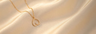 Side view of a heart-shaped lab-grown diamond pendant necklace in 14 KT yellow gold, featuring an open heart motif with a floating round brilliant diamond on a delicate chain.
