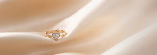 A Réia white gold ring featuring a heart-shaped lab-grown diamond center stone flanked by round lab-grown diamonds, resting on beige fabric.