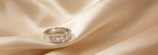 A Réia white gold band ring with a modern, angular, and faceted design, is displayed on a gray surface with strong shadows.
