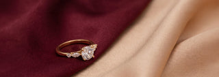 A Réia yellow gold solitaire ring with a six-prong setting and a round lab-grown diamond, resting on beige fabric.