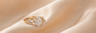 A Reia yellow gold solitaire engagement ring featuring a large oval lab-grown diamond in a four-prong setting, displayed on satin fabric.