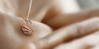 Réia rose gold swan pendant necklace with lab-grown diamonds, displayed on champagne fabric.