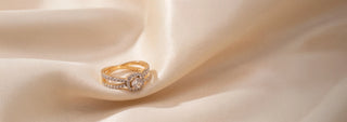 A Réia yellow gold three-stone ring with a round center lab-grown diamond and two lab-grown diamond side stones, resting on beige fabric with blurred flowers.