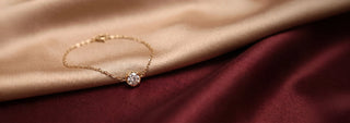 Angled view of Solitaire Diamond Bracelet in 14KT Yellow Gold, featuring a bezel-set round lab-grown diamond on a delicate chain. Captured against a beige and burgundy satin backdrop, radiating timeless elegance.