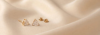 Réia pair of yellow gold stud earrings with round brilliant lab-grown diamonds, displayed on beige fabric.