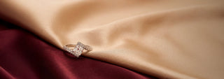 A Réia white gold solitaire ring with a round lab-grown diamond in a tension setting, resting on draped pale neutral satin fabric.